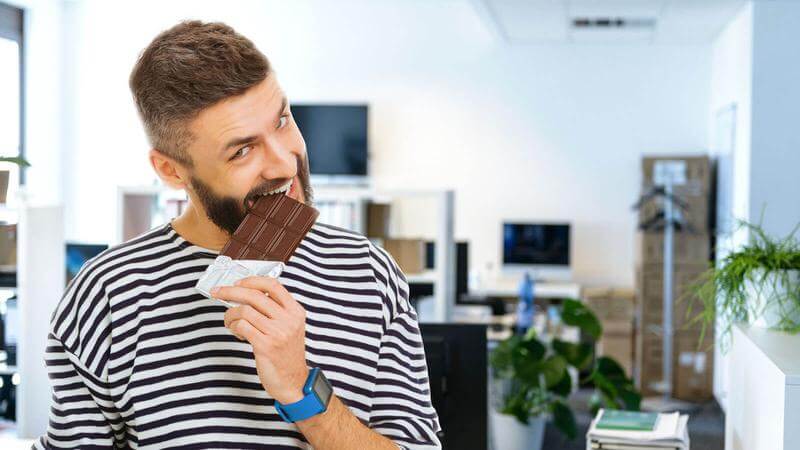 Mann beißt im Büro in Schokolade