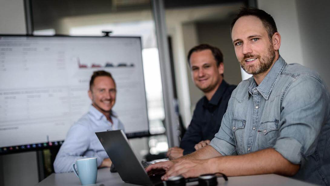 3 Männer arbeiten im Büro an einem Laptop